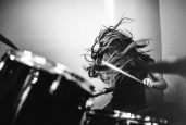 A 9 year old girl has fun playing a drum set in her room, working on songs for her band.  High contrast black and white image.