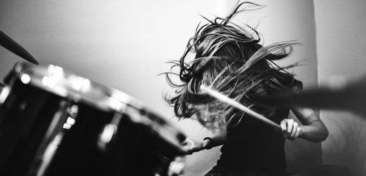 A 9 year old girl has fun playing a drum set in her room, working on songs for her band.  High contrast black and white image.